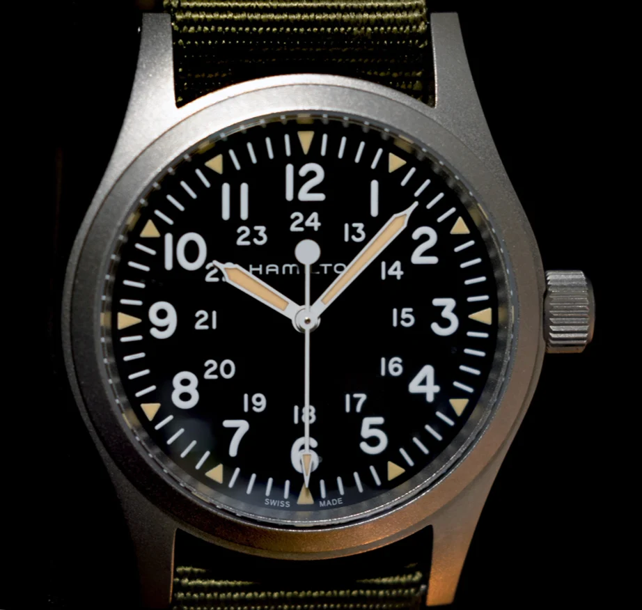 The Khaki Field Mechanical dial straight on: black, large white numerals 1 to 12 with a smaller ring of 13 to 24 inside, triangle markers at each hour, a white lume dot at twelve and Swiss Made at six.