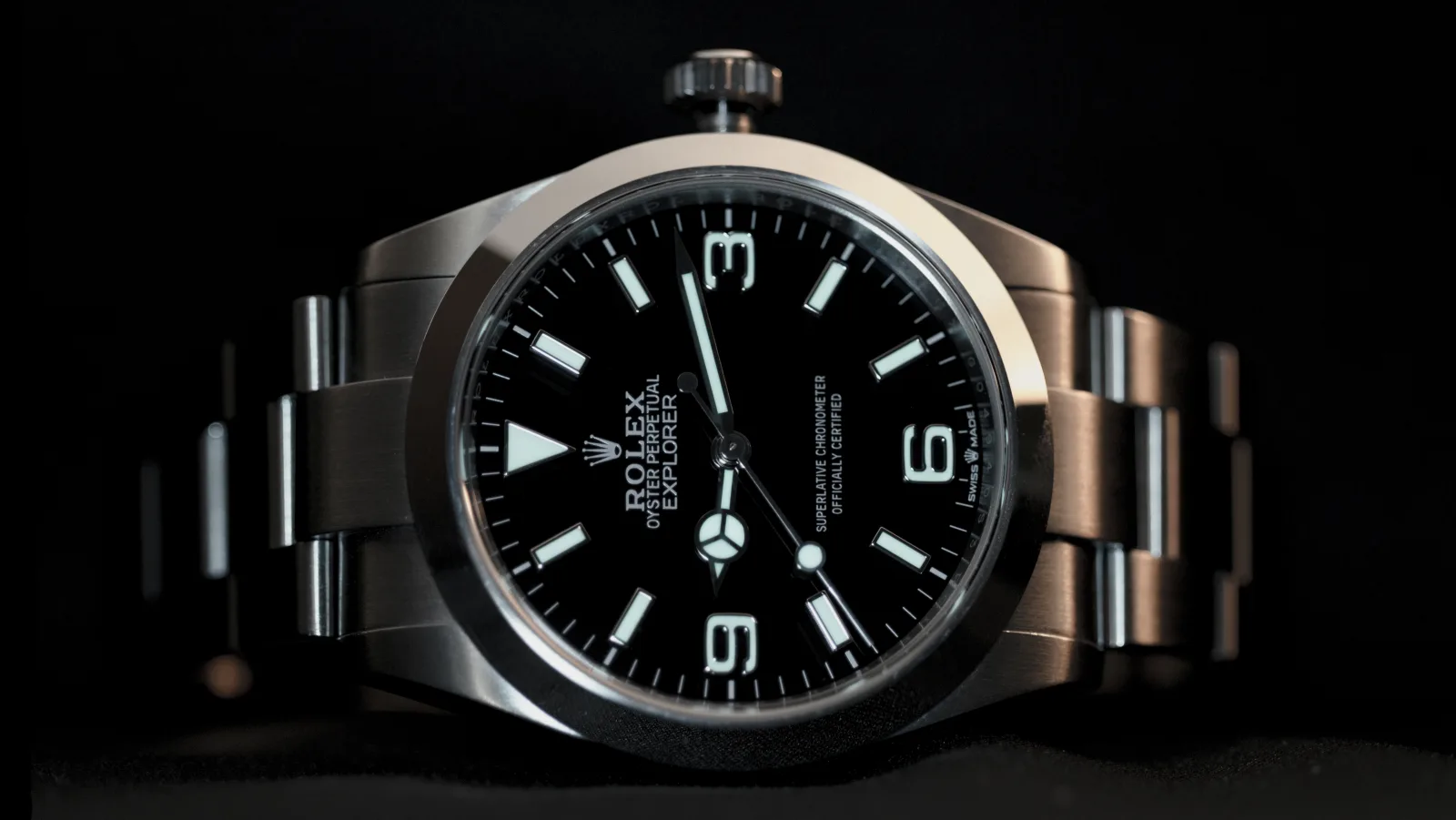 Rolex Explorer on its steel Oyster bracelet, seen at an angle against black: black dial, 3, 6 and 9 numerals, triangle at twelve.
