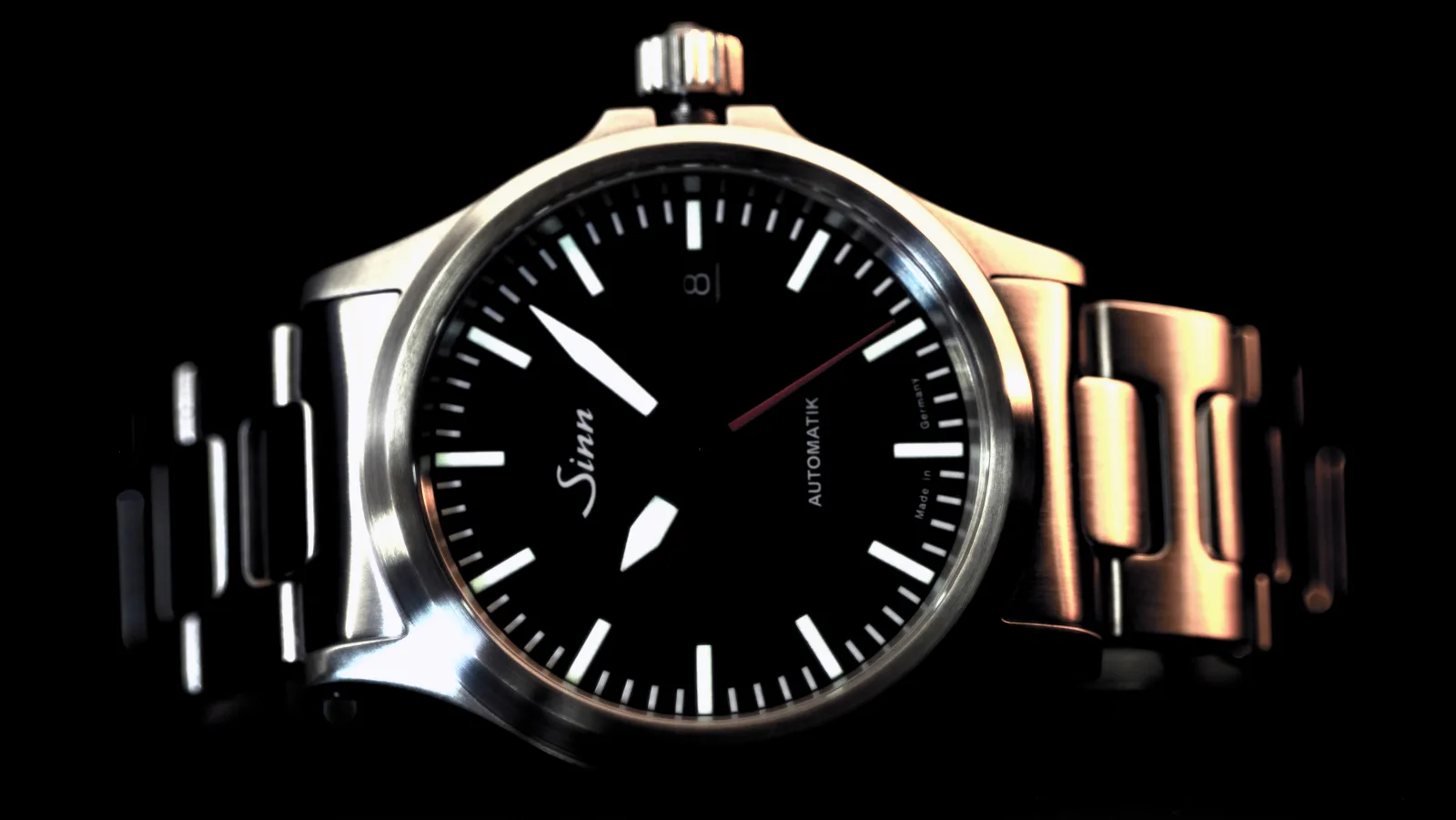 Sinn 556 I RS on its steel bracelet, seen at an angle against black: black dial, white markers, red seconds hand.